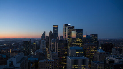 Fototapeta premium City skyline at dusk with tall modern skyscrapers illuminated against warm gradient sky, showing urban development and vibrant city life at twilight.