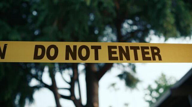 Yellow caution tape do not enter against trees and sky daytime shows restricted access area safety and perimeter control in outdoor environment
