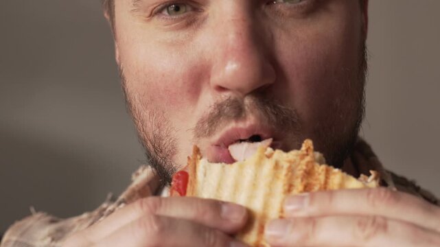 A man eats a delicious-looking sandwich made with melted cheese.