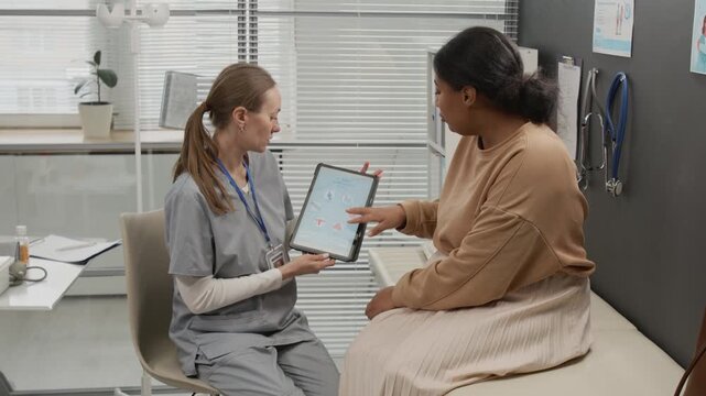 Fertility specialist in grey scrubs holding digital tablet and answering womans questions about IVF treatment cycles