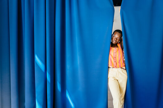 Black woman emerging between blue curtains with orange outfit color contrast
