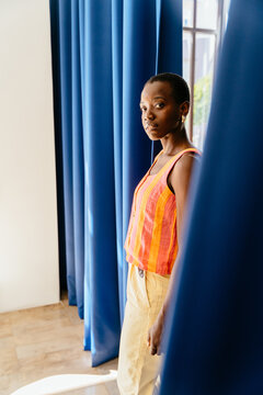 Black woman framed by blue curtains with orange outfit color contrast