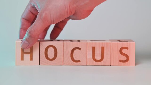 A hand rearranges wooden blocks to spell words related to focus and hocus. This activity showcases the interaction with simple materials in a neutral setting