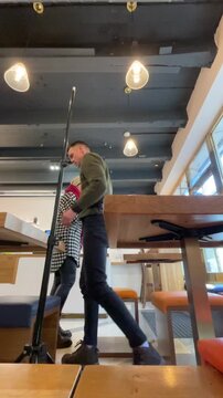 Woman and man meeting at high table, vertical stock video capturing lowangle interior with houndstooth coat back view, tripod and camera gear visible, candid conversation