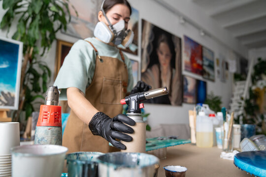 Concentrated craftswoman in protective respirator on face working with epoxy resin at home workshop, special equipment providing protection from inhaling varnish, female creating art from epoxy.