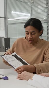 Vertical view of African American young woman pointing at medical records while discussing reproductive health with Caucasian female fertility specialist