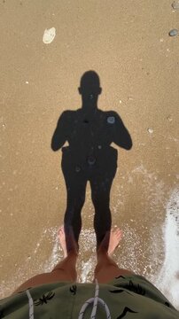 Shadow of a man on the beach shore watching waves breaking peacefully over his feet