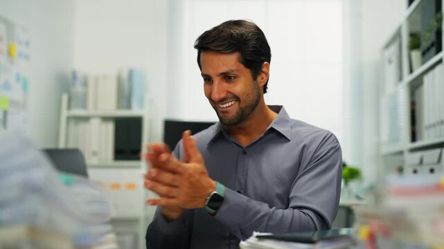 Hispanic employee indoors, multitasking on computer, overwhelmed by technology and paperwork, showing stress.