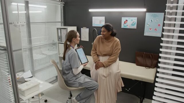 Female medical specialist with digital tablet discussing IVF procedure with positive woman during appointment in clinic