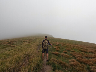 Obraz premium Lone Hiker with Backpack Walking into Dense Mist on Mountain Ridge