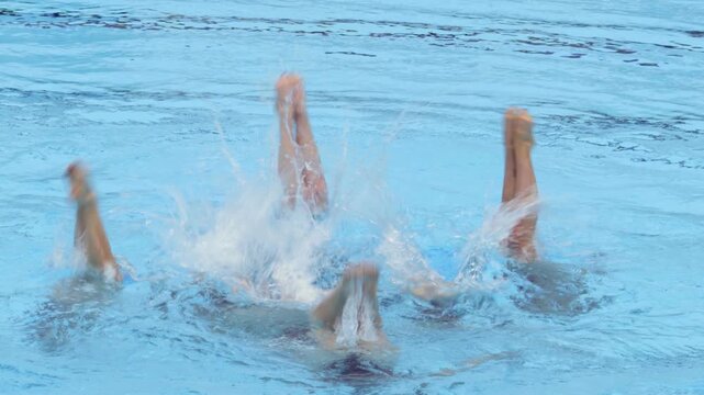 Artistic swimmers performing synchronized leg choreography in blue swimming pool water, showcasing teamwork, grace, athletic skill and summer aquatic sport performance