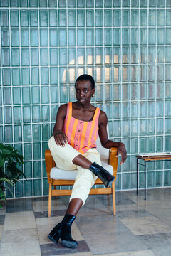 Detached Black woman sitting in minimalist interior with glass block wall