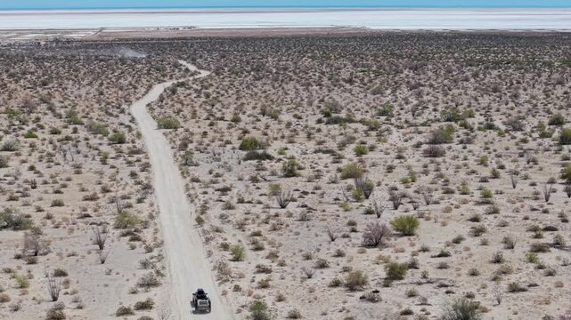 An SUV pulls a teardrop camper trailer through the Baja desert, approaching the El Salar salt flats in Baja California under clear skies.