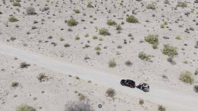 SUV drives along a dirt road with a teardrop camper trailer in the Baja desert near El Salar salt flats in Baja California.