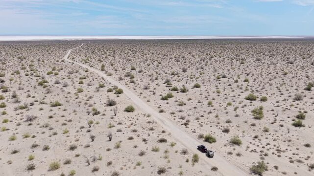 An SUV pulls a teardrop camper trailer along a dirt road in the Baja desert near the El Salar salt flats, showcasing the landscape.