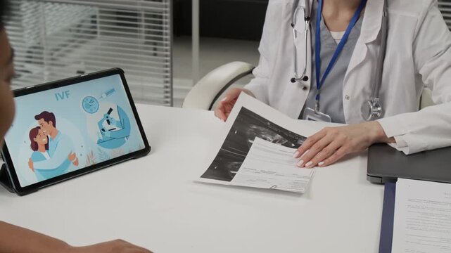 African American woman handing ultrasound results to Caucasian IVF expert who giving her comment after having look at them during consultation