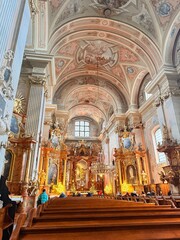 Fototapeta premium Ornate Baroque Church Interior with Gold Altar Ceiling Frescoes and Visitors