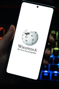 Punta Arenas, Chile &ndash; April 30, 2026: A person holding a smartphone displaying the Wikipedia logo and slogan on a white screen with a colorful backlit mechanical keyboard in the background