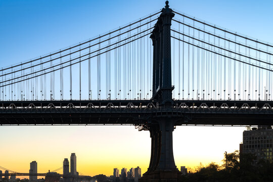 The silhouette of the Manhattan bridge stands against the vibrant glow of the horizon during the early morning hours.