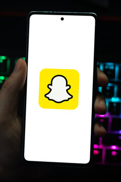 Punta Arenas, Chile &ndash; April 30, 2026: A person holding a smartphone displaying the yellow Snapchat ghost logo on its screen with a vibrant, colorfully backlit mechanical keyboard in the background