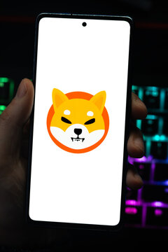 Punta Arenas, Chile &ndash; April 30, 2026: A hand holding a smartphone displaying the Shiba Inu (SHIB) cryptocurrency logo on its screen with a vibrant, colorfully backlit mechanical keyboard in the backgr
