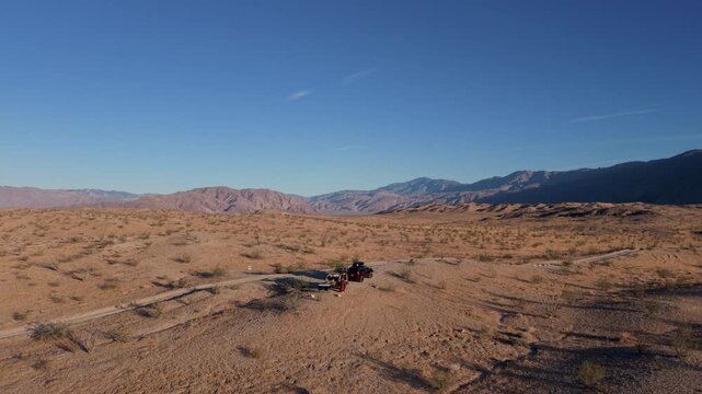 Aerial view shows SUV and teardrop camper parked in Anza Borego Desert. The location features open desert land and mountains.