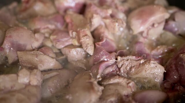 Fresh chicken liver pieces sizzle and brown in a hot frying pan with bubbling oil during a detailed meal preparation process. Concept of home cooking, healthy protein, and offal preparation.