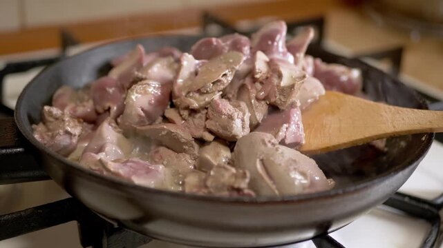 Chicken livers and gizzards sizzle in a hot frying pan on a gas stove during home meal preparation. Concept of healthy protein, home cooking, traditional cuisine, and nutritious dinner.