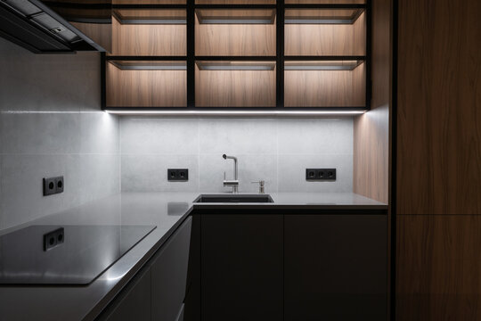 Modern minimalist kitchen interior with black cabinets, wooden upper shelves, built in lighting, sleek sink area and contemporary apartment design
