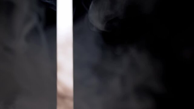 A bright vertical beam of light shines through drifting smoke against a dark background. Concept of mystery, dramatic lighting, unknown portals, and abstract atmospheric backgrounds.