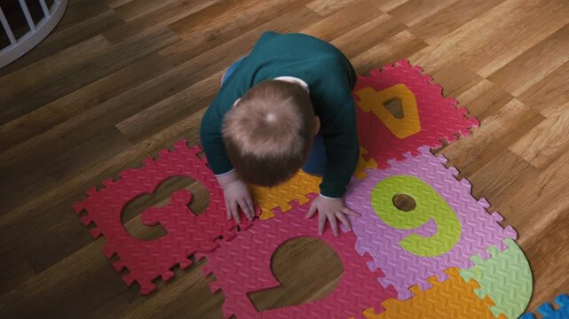 Top view of a little boy connecting colorful foam number puzzle pieces on the floor
