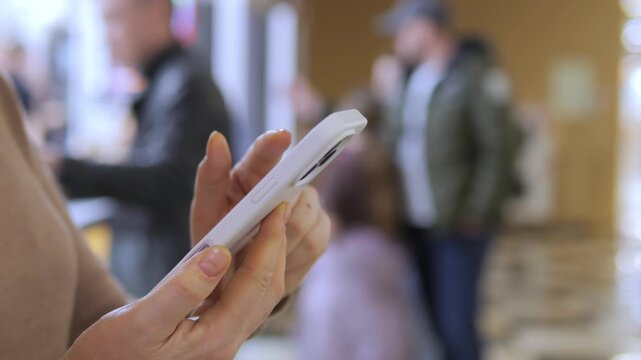 Close-up of hand holding smartphone. Background blurred with people walking. Urban setting with natural lighting. Focus remains on phone interaction