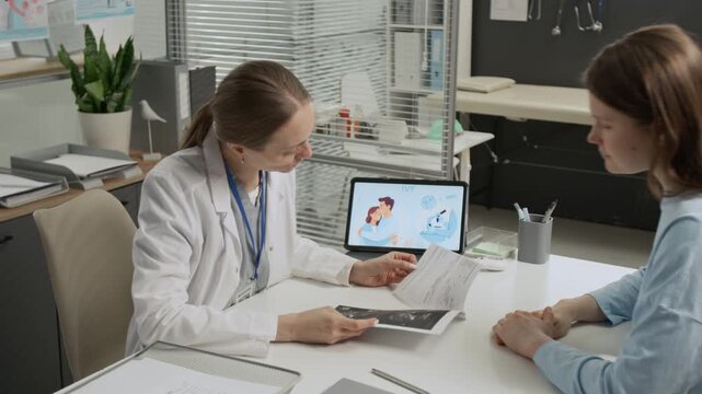 Zoom in view of young female patient giving ultrasound results to IVF expert examining and discussing them with her during preconception appointment