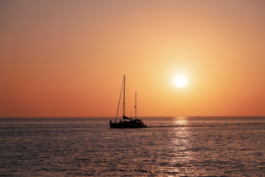 The serene ocean glows with the last light of day as a catamaran journeys onward, silhouetted against the warm, vibrant colors of dusk, a beautiful maritime scene.