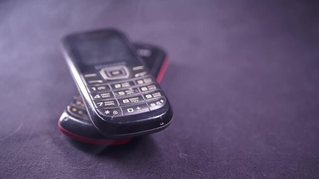 Two vintage button mobile phones rest on a dark surface while white smoke drifts slowly around them. Concept of obsolete technology, electronic waste, and overheating battery hazards.