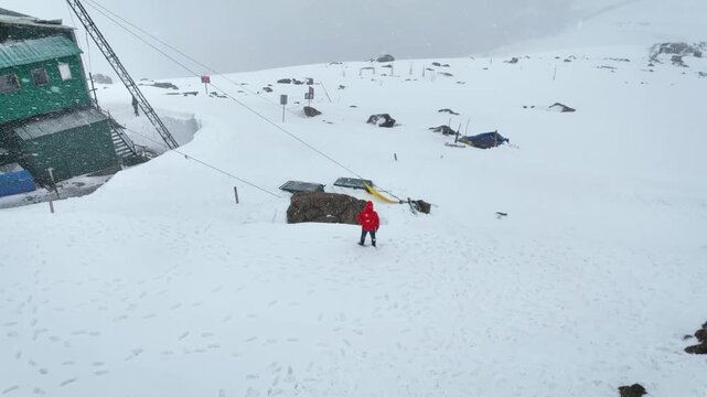Drone orbit revealing Orange jacket Traveller at snow-covered Phase 2 Gondola station in Gulmarg.