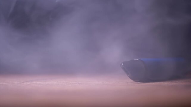A close-up of a blue disposable electronic cigarette lying on wood while releasing thick white vapor into the dark. Concept of nicotine addiction, vaping trends, and unhealthy habits.