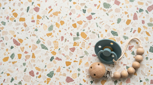 Blue Silicone Baby Pacifier and Natural Wooden Bead Pacifier Clip Accessory on Modern Colorful Terrazzo Background Surface, Minimalist Sustainable Baby Gear for Soothing and Comforting Infants, Child