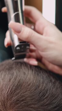 Close-up of barber using electric clippers to trim mans hair, precise grooming process in barbershop focusing on clean fade haircut and professional styling