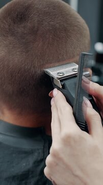 Close-up of barber using electric clippers to trim mans hair, precise grooming process in barbershop focusing on clean fade haircut and professional styling