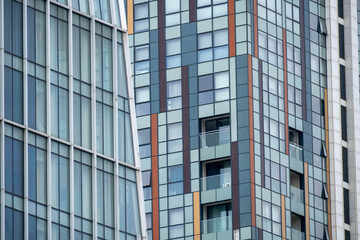 Fototapeta premium Close-up view of modern glass high-rise buildings with geometric facades, windows and balconies, showing urban architecture and abstract city patterns.