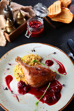 Baked duck leg with cherry sauce. An exquisite dish. Slices of white bread. Cherry sauce in small jar. Top view.