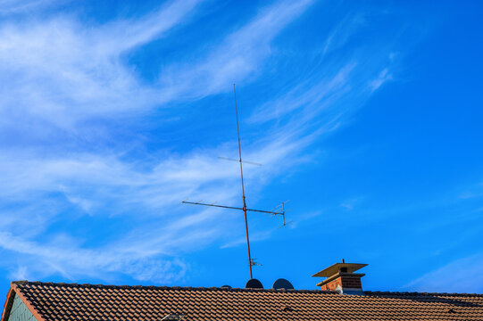 Clear blue sky with an antenna atop a roof and wispy clouds