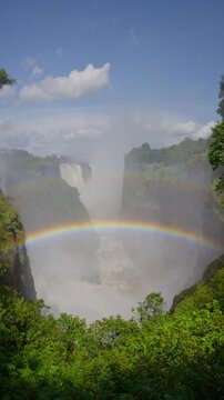 Spectacular rainbow arching over magnificent Victoria Falls on Zambezi River, famous landmark located on Zambia and Zimbabwe border in southern Africa