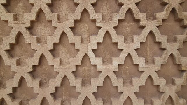 Close-up view of an ornate mosque wall in Morocco featuring intricate geometric Islamic patterns carved in warm-toned stone.