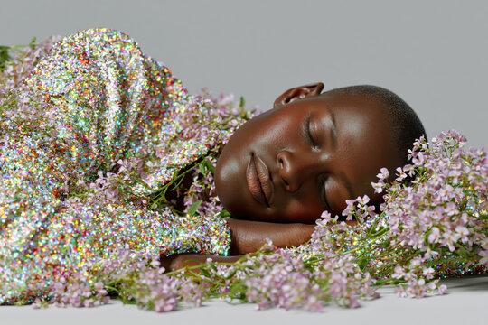 Peaceful woman with closed eyes resting among delicate pink flowers and shimmering glitter on a light background