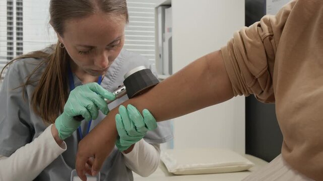 Female dermatologist examining skin lesions on womans arm with help of dermatoscope during medical consultation
