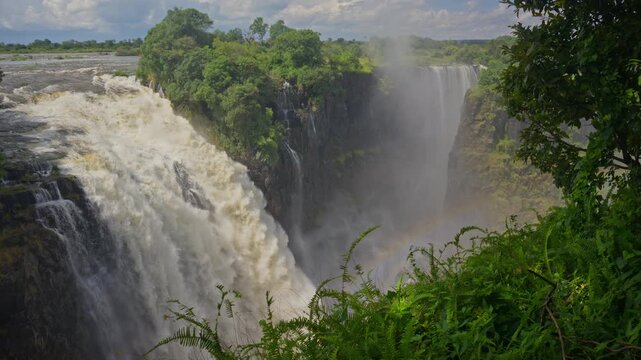 Victoria Falls roaring with powerful water creating mist and rainbow on Zambezi River, forming border between Zimbabwe and Zambia on southern african continent