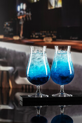 Fototapeta premium Close-up of colorful cocktail with blue Curacao in interior of restaurant or cafe. Refreshing drink with blue syrup. Blue lagoon drink with blue curacao at bar counter close up. Tall wine glasses
