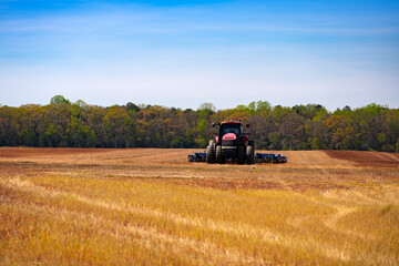 Fototapeta premium Agriculture fieldwork. Agricultural field landscape. Farm field with tractor. Farmland machinery. Plowed field tractor. Tilled field equipment. Rural farm scene.